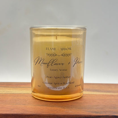 A clear glass candle jar with a label that reads 'Flame Arrow Moonflower Pear Luxury Aroma', with additional scent notes listed below.