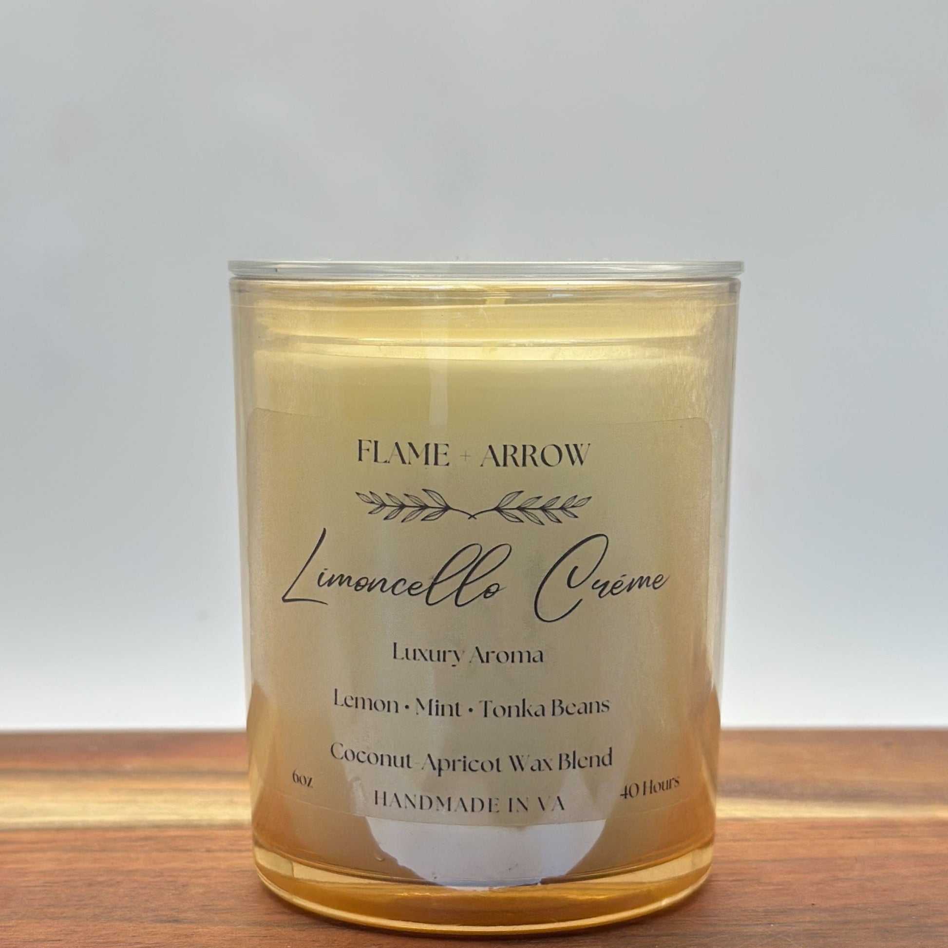 A clear glass candle jar with a label that reads 'Flame Arrow Limoncello Crème Luxury Aroma', with additional scent notes listed below.