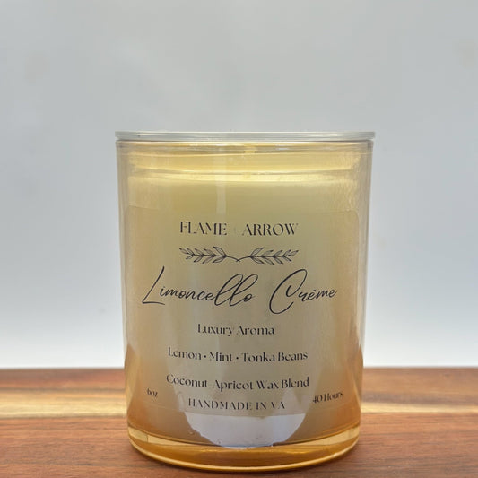 A clear glass candle jar with a label that reads 'Flame Arrow Limoncello Crème Luxury Aroma', with additional scent notes listed below.