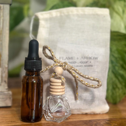 A bottle of car diffuser refill oil next to an empty bamboo cork diffuser in front of a canvas Flame and Arrow bag.