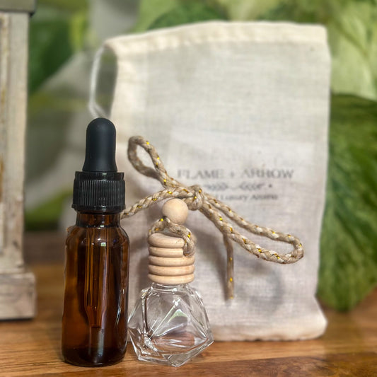 A bottle of car diffuser refill oil next to an empty bamboo cork diffuser in front of a canvas Flame and Arrow bag.